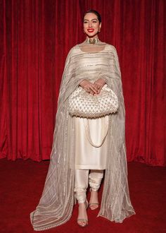 a woman standing in front of a red curtain wearing a white outfit and holding a purse