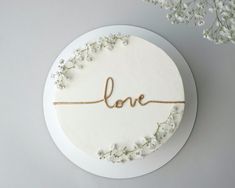 a white cake with the word love written on it and flowers in front of it