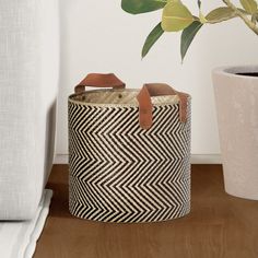 a black and white basket sitting on top of a wooden floor next to a potted plant