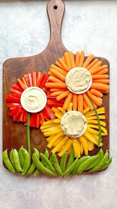 a cutting board with carrots, peppers and dip