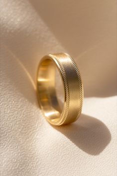 a gold wedding ring sitting on top of a white cloth covered surface with sunlight coming through the window