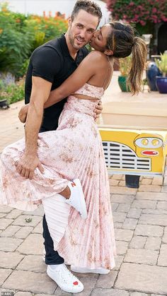 a man and woman kissing on the cheek in front of a yellow bench with flowers