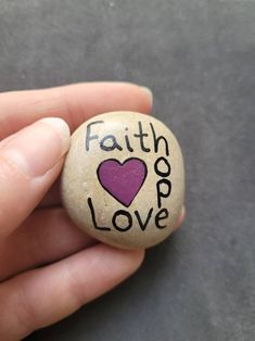 a hand holding a rock with the word faith love painted on it and a heart