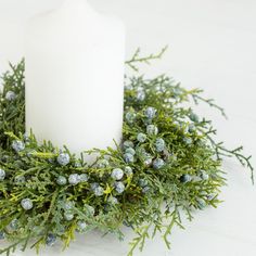 a white candle is surrounded by greenery and pine cones