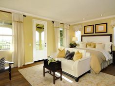 a large bedroom with yellow walls and white furniture in the room, along with two windows