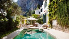 an outdoor swimming pool with lounge chairs and umbrellas in front of a mountain side house