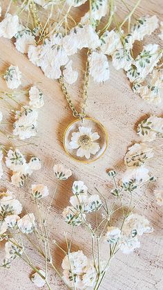 the necklace is surrounded by white flowers and greenery on a wooden surface with gold chain