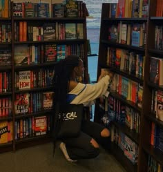 a woman kneeling down in front of a book shelf filled with books