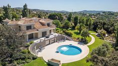 an aerial view of a house with a swimming pool in the foreground and trees surrounding it