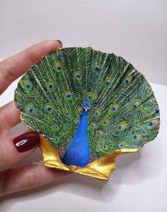 a hand holding a green and blue peacock ornament