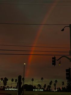 a rainbow is seen in the sky over palm trees and traffic lights at night time