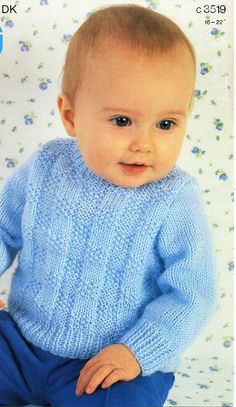 a baby wearing a blue sweater sitting on top of a white sheet with flowers in the background