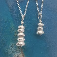 two silver necklaces sitting on top of a blue surface, one is dangling from a chain