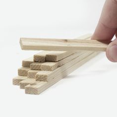 a hand holding a piece of wood next to several pieces of wooden dows on a white background