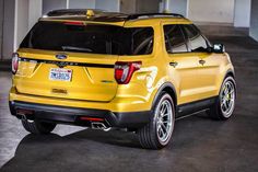 the rear end of a yellow ford explorer parked in a parking garage with no one around