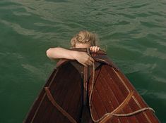 a woman sitting on top of a wooden boat in the water with her arms crossed