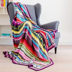 a colorful crocheted blanket sitting on top of a gray chair next to a book shelf