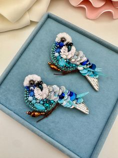 two blue and white bird brooches sitting on top of a blue velvet box