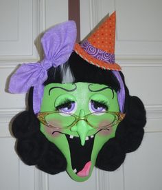 a green and black mask with a purple bow on it's head is hanging from a door