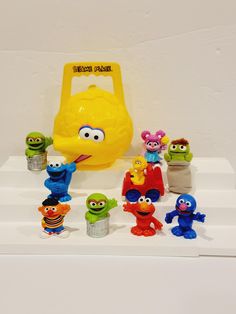 an assortment of sesame street toys on display in front of a yellow plastic object with characters around it