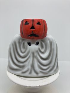 a ceramic pumpkin head sitting on top of a white bowl with black eyes and mouth