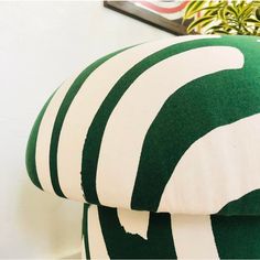 a green and white striped ottoman cushion sitting on top of a wooden table next to a potted plant