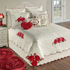 a white bed with red flowers on it in a room next to a dresser and rug