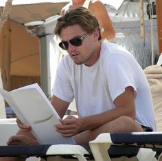 a man sitting on top of a white chair next to an open book in his hands