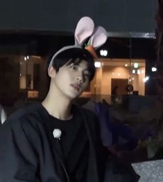 a young man wearing a bunny ears hat sitting in front of a building at night