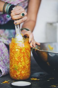 a woman is pouring orange liquid into a glass jar with a spoon in front of her