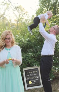 a man holding a baby up in the air while standing next to a woman wearing a dress