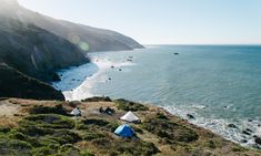 tents are pitched up on the side of a cliff by the ocean