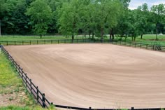 an empty dirt paddock with trees in the background