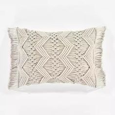 a white knitted pillow with fringes on the front and back, against a white background