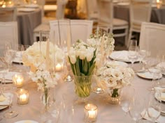 a table with white flowers and candles in vases on top of the tables at a wedding reception