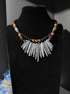 Beautiful tribal style choker necklace with an ethnic touch. The necklace is made of irregular kyanite sticks and blue sunstone beads. Afterwards there are also agate beads and fine glass beads. The necklace in the central part is double stranded. The necklace is a crew neck, 48cm long with an adjustable clasp with a 5cm extension. The necklace is in shades of blue, gray and bronze which makes it very elegant. It is a particular necklace, for those who love handmade pieces. The necklace is very elegant, very beautiful in summer with a low-cut dress. All jewels are delivered in a decorated box, ready to be given as a gift to your loved one. How to take care of your jewellery: put on your beauty products (cosmetics, perfumes, ...) before wearing your precious jewel. Clean your jewelry with a Handmade Kyanite Healing Necklaces, Handmade Bohemian Kyanite Jewelry, Bohemian Blue Necklace With Raw Stone, Blue Sunstone, Blue And Bronze, Low Cut Dresses, Stones Necklace, Bronze Necklace, Cut Dress