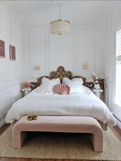 a bedroom with white walls and wood flooring has a pink ottoman on the bed