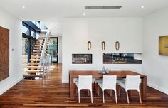 a dining room table with white chairs next to a stair case in a modern home