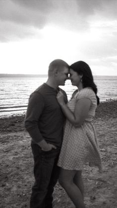 a man and woman standing next to each other on a beach with the ocean in the background