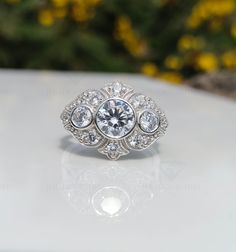 a diamond ring sitting on top of a white surface with yellow flowers in the background