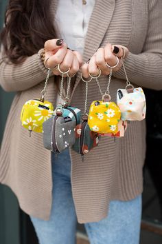 a woman is holding four small purses in her hands, one has a cat keychain on it