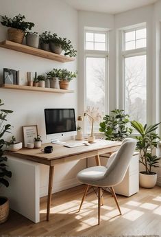 a desk with a computer and some plants on it in front of two large windows