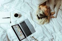 a woman laying on top of a bed next to a laptop computer and eyeglasses