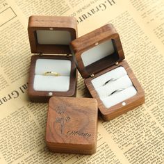 three wooden boxes with wedding rings in them on top of a newspaper page next to an open ring box