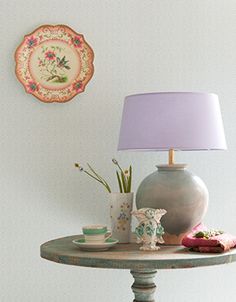 a table with a lamp, vase and other items on it next to a wall