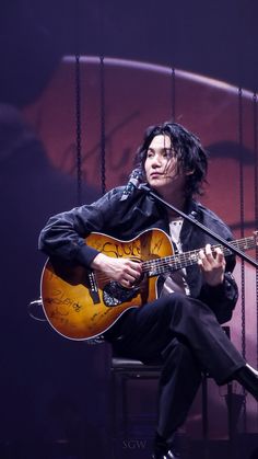 a man sitting on top of a chair holding a guitar in front of a microphone