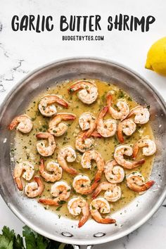 garlic butter shrimp in a skillet with parsley on the side and lemon wedges next to it