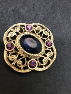 1928 Jewelry Company Victorian Brooch Blue Oval Faceted Glass Center, Purple Rhinestone Sets Filigree Style Quatrefoil Gold Finish Setting Victorian Revival Jewelry Set 1928 Jewelry Company Pressed Back Gold Tone Filigree Settings, Findings Vintage from 1970's-80's Size: 1 3/4 x 1 3/4 inches Condition: Very good; slight finish loss on pin back. Will be shipped First Class Mail in a gift box Blue Oval Brooch Jewelry, Oval Blue Brooch Jewelry, Oval Blue Brooch, Elegant Oval Blue Brooches, Elegant Blue Oval Brooches, Blue Oval Brooch For Gifts, Blue Oval Brooch, Vintage Sapphire Brooch Jewelry, Ornate Oval Brooch For Formal Occasions