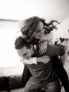 a man carrying a woman on his back in the living room while she smiles at her