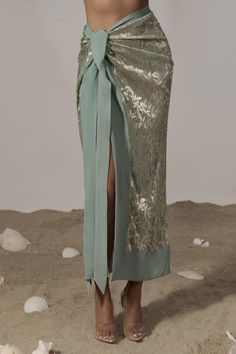 a woman standing on the beach wearing a green skirt with gold sequins around it